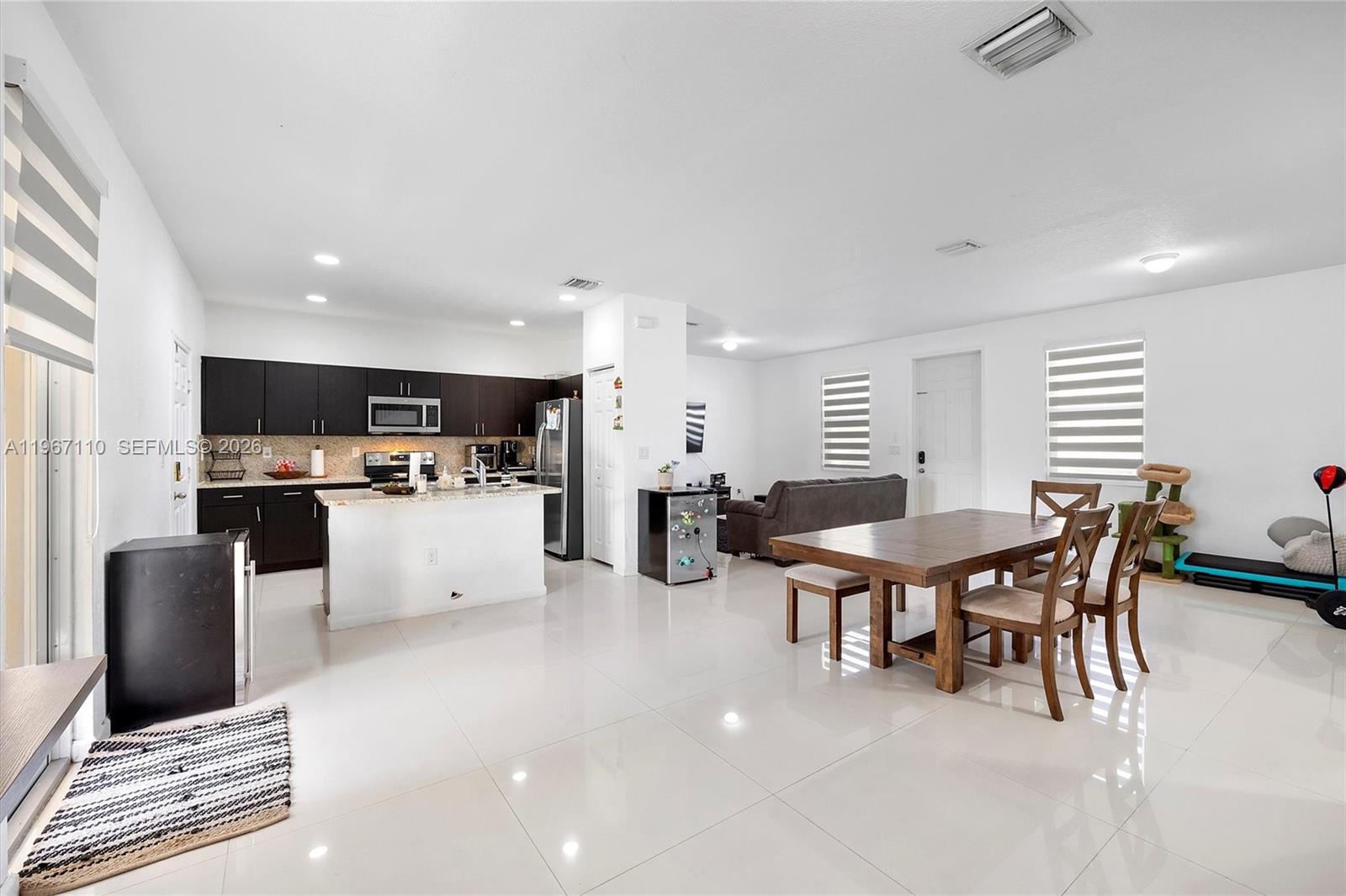 An open-concept kitchen and dining area features dark cabinetry, a kitchen island, and tile flooring — 24557 SW 117th Ave, Homestead FL 33032, HOMESTEAD, FL