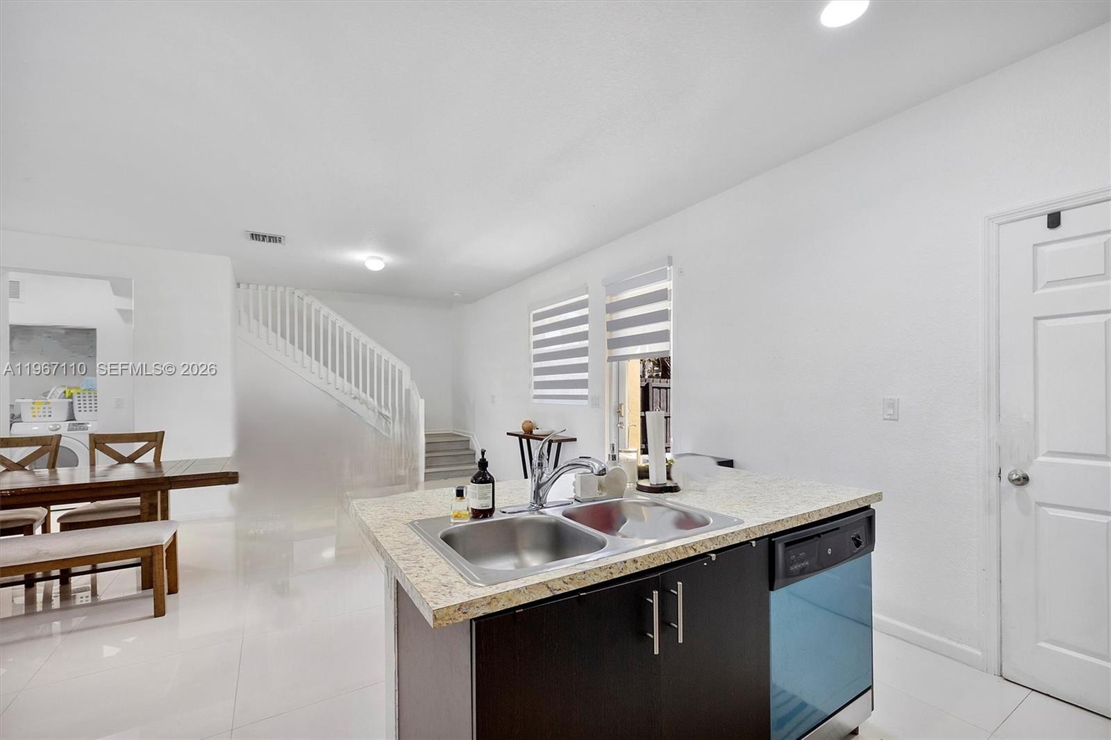 A kitchen island with a double sink sits before a dining area and staircase — 24557 SW 117th Ave, Homestead FL 33032, HOMESTEAD, FL