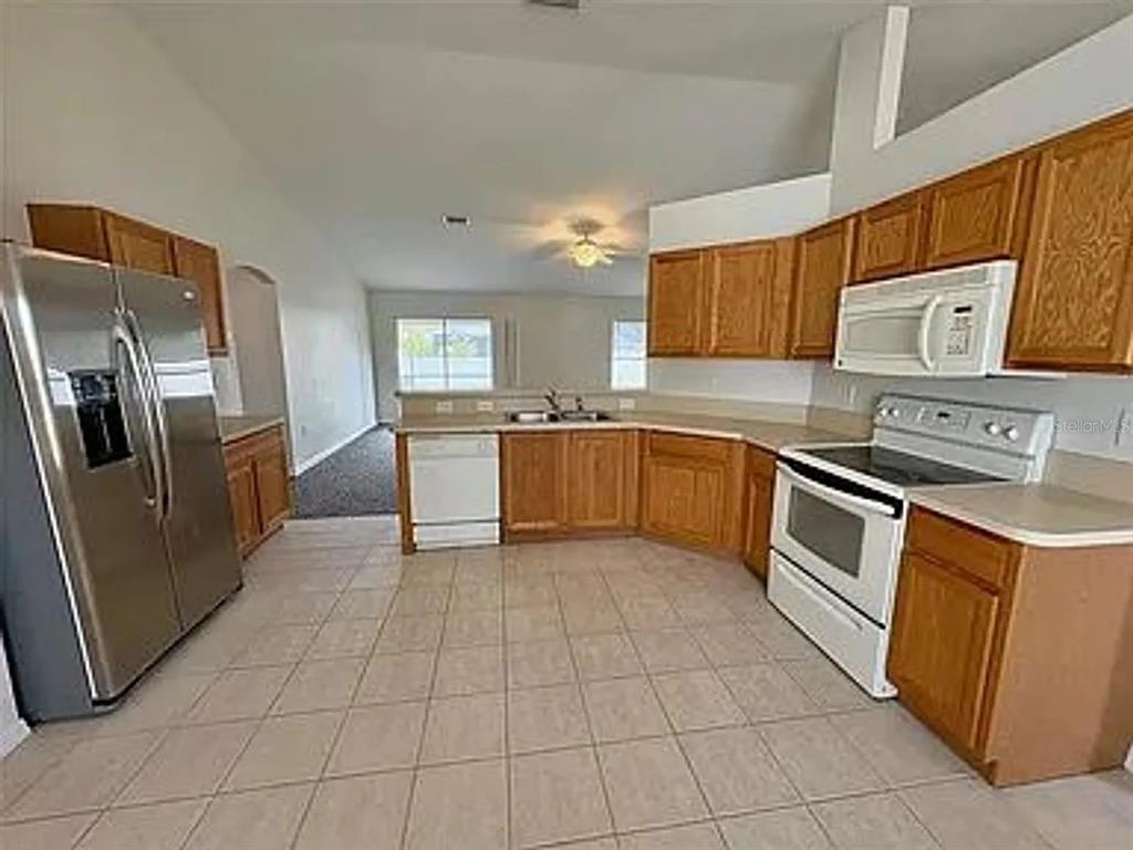 A kitchen features wood cabinets, white appliances, a stainless steel refrigerator, and tiled flooring — 2399 ORACLE LANE, NORTH PORT, FL