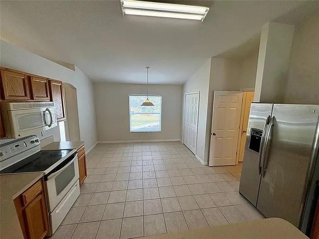 A kitchen with tile flooring, wood cabinets, stainless steel appliances, and a dining area — 2399 ORACLE LANE, NORTH PORT, FL