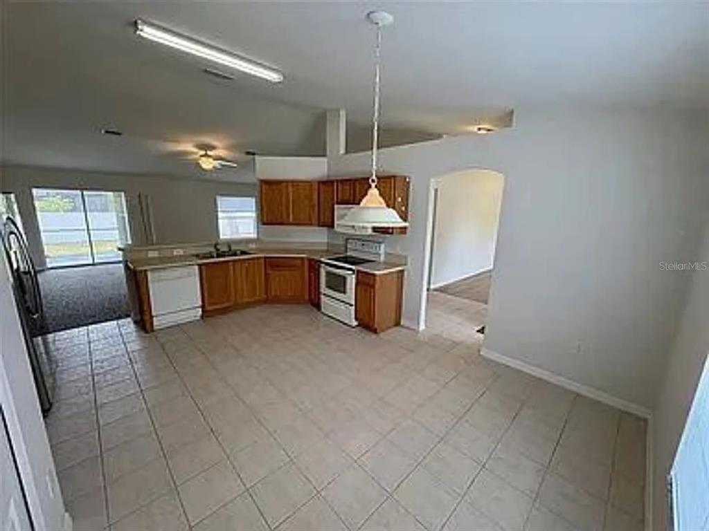 A kitchen with wood cabinets, white appliances, and tile flooring opens to a living area — 2399 ORACLE LANE, NORTH PORT, FL