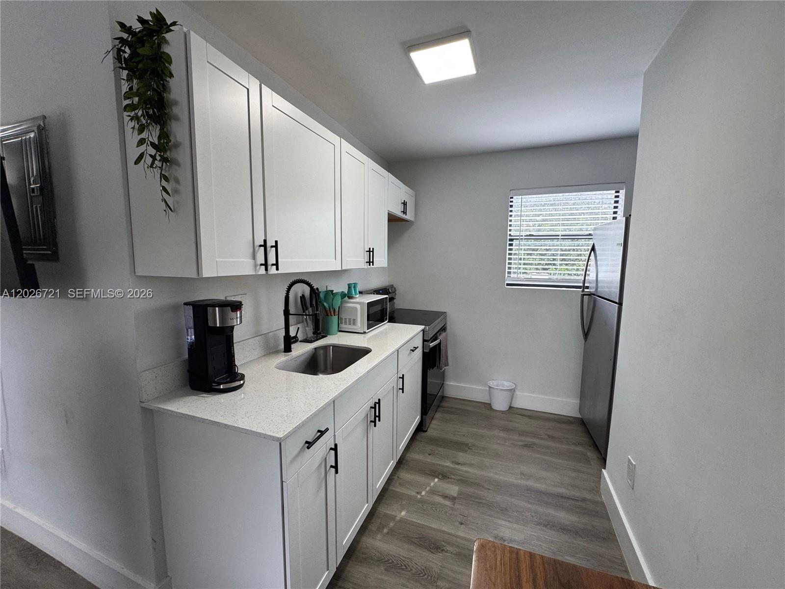 A small kitchen features white cabinets, quartz countertops, stainless steel appliances, and wood-look flooring — 584 NW 30th St # 3, Miami FL 33127, MIAMI, FL