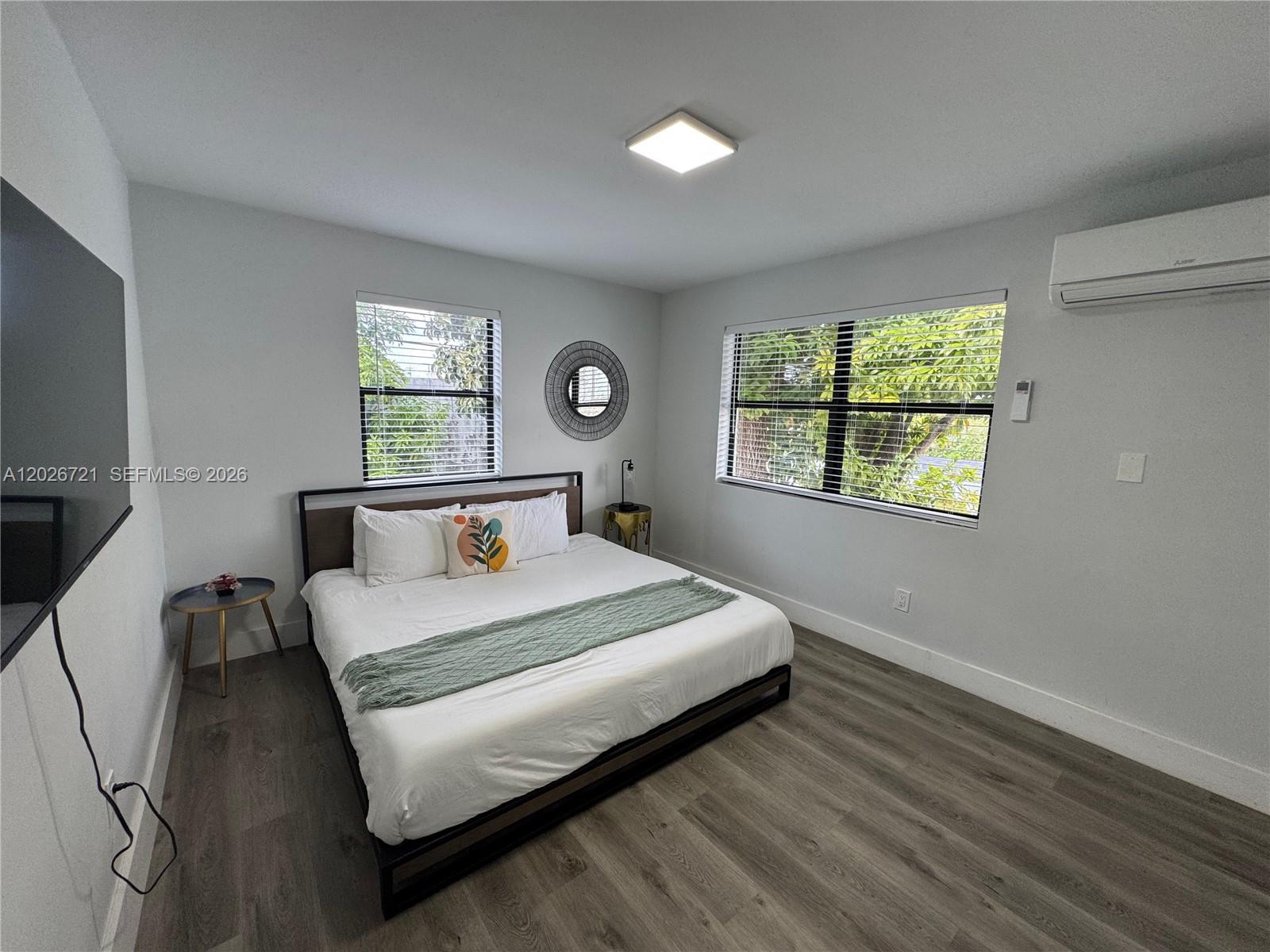 A bedroom features a bed, two windows, a wall-mounted television, and wood-look flooring — 584 NW 30th St # 3, Miami FL 33127, MIAMI, FL