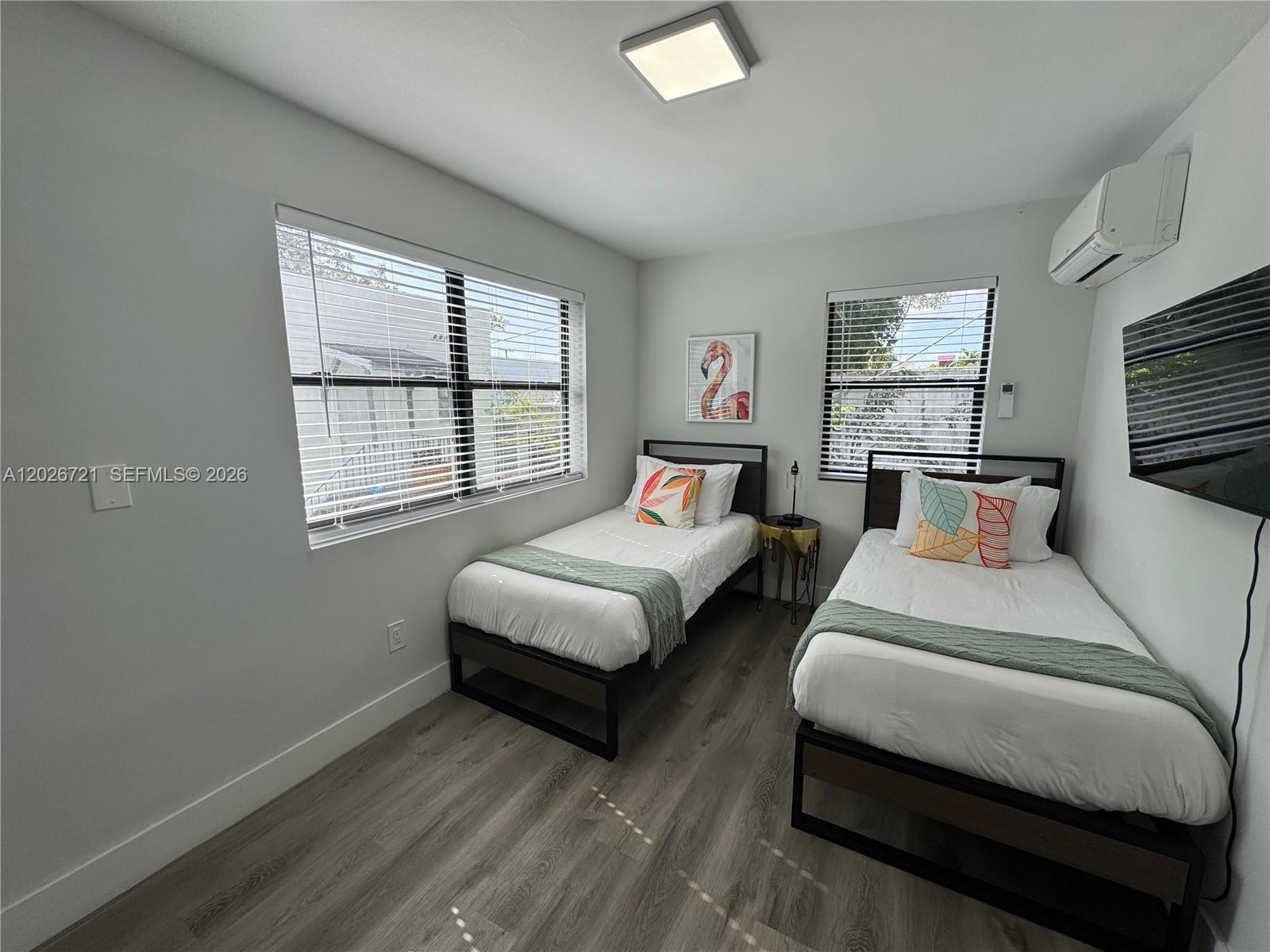 A bedroom features two twin beds, wood-look flooring, white walls, and two windows with blinds — 584 NW 30th St # 3, Miami FL 33127, MIAMI, FL
