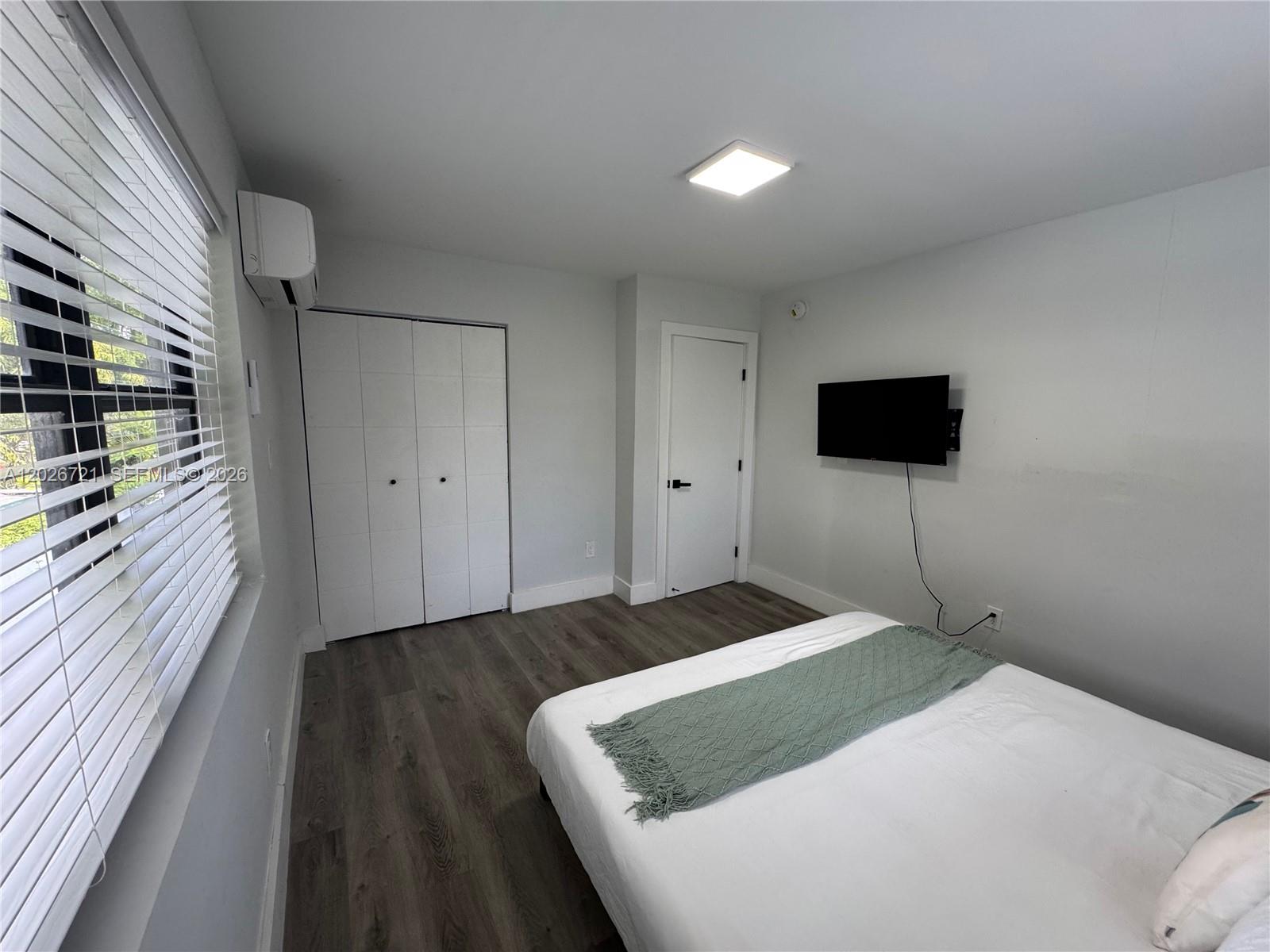A bedroom features white walls, wood-look flooring, a wall-mounted television, and a closet — 584 NW 30th St # 3, Miami FL 33127, MIAMI, FL