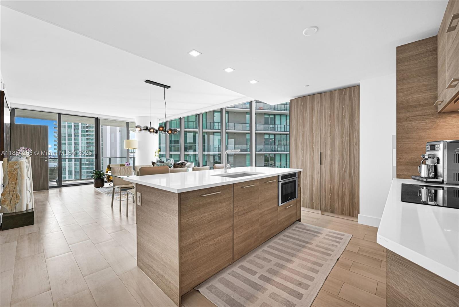 A modern kitchen features a wood-paneled island, white countertops, and floor-to-ceiling windows overlooking city buildings — 650 NE 32nd St # 2201, Miami FL 33137, MIAMI, FL