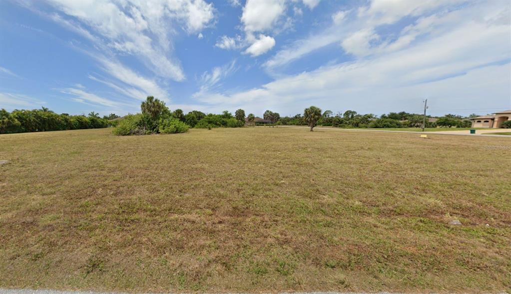 A wide, grassy vacant lot under a blue sky with scattered clouds and palm trees — 103 BONITA DRIVE, ROTONDA WEST, FL