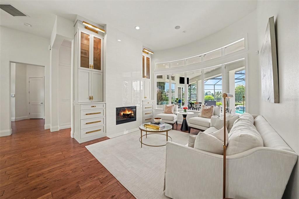A living room features a fireplace, built-in cabinetry, a sofa, and large curved windows — 3450 FOXMEADOW COURT, LONGWOOD, FL