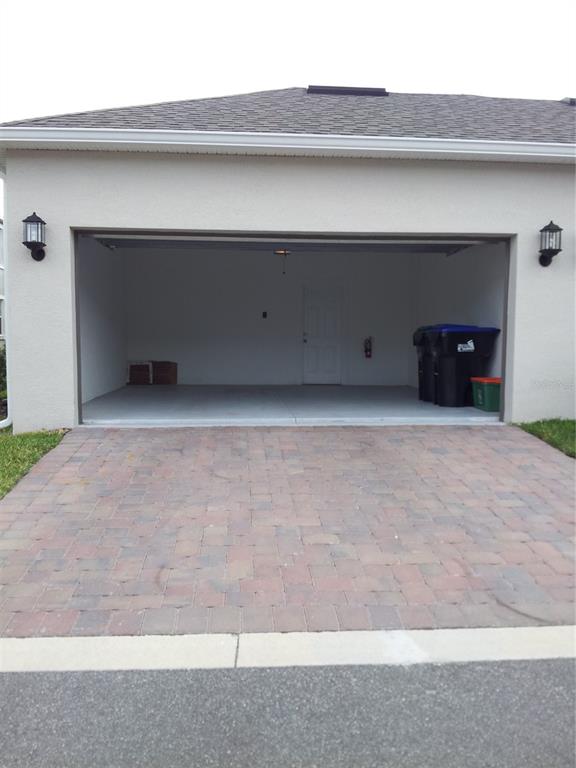 An open garage with a paver driveway, white walls, and two outdoor wall lanterns — 7324 ELLA LANE, WINDERMERE, FL