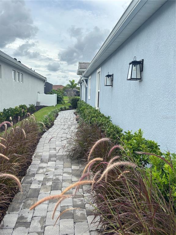 A paved walkway leads between two houses with blue and grey stucco exterior walls — 16117 ISOLA PLACE, BRADENTON, FL