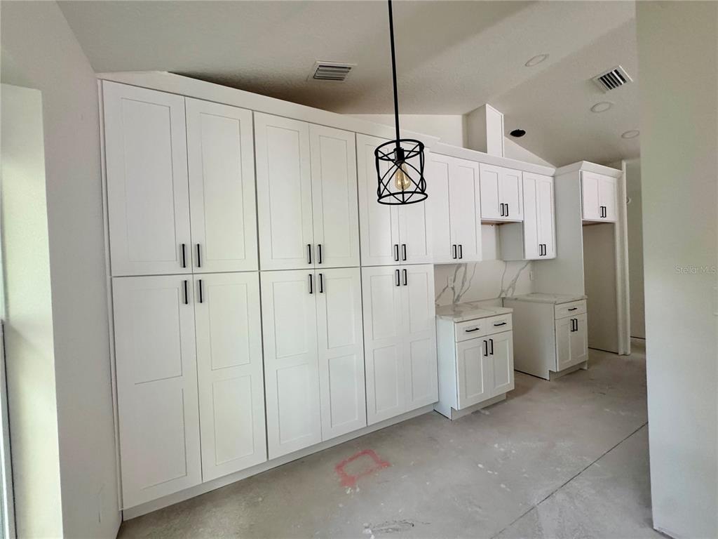 A galley kitchen features white cabinets, marble-look countertops, and light wood flooring — 2017 E SEWARD STREET, TAMPA, FL
