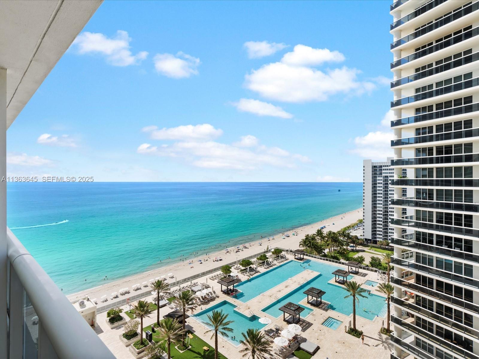 A high-angle view from a balcony overlooking a swimming pool deck and the ocean — 1830 S Ocean Dr, Hallandale Beach FL 33009, HALLANDALE BEACH, FL