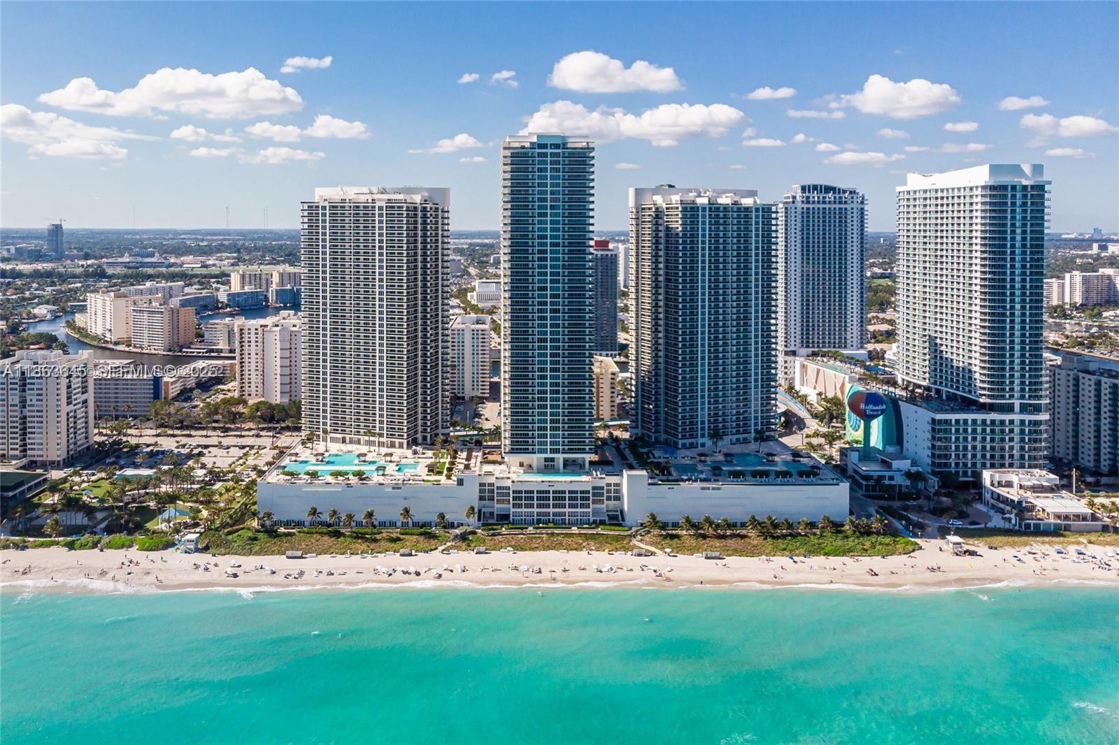 An aerial view shows several tall residential towers situated directly along a sandy beach — 1830 S Ocean Dr, Hallandale Beach FL 33009, HALLANDALE BEACH, FL