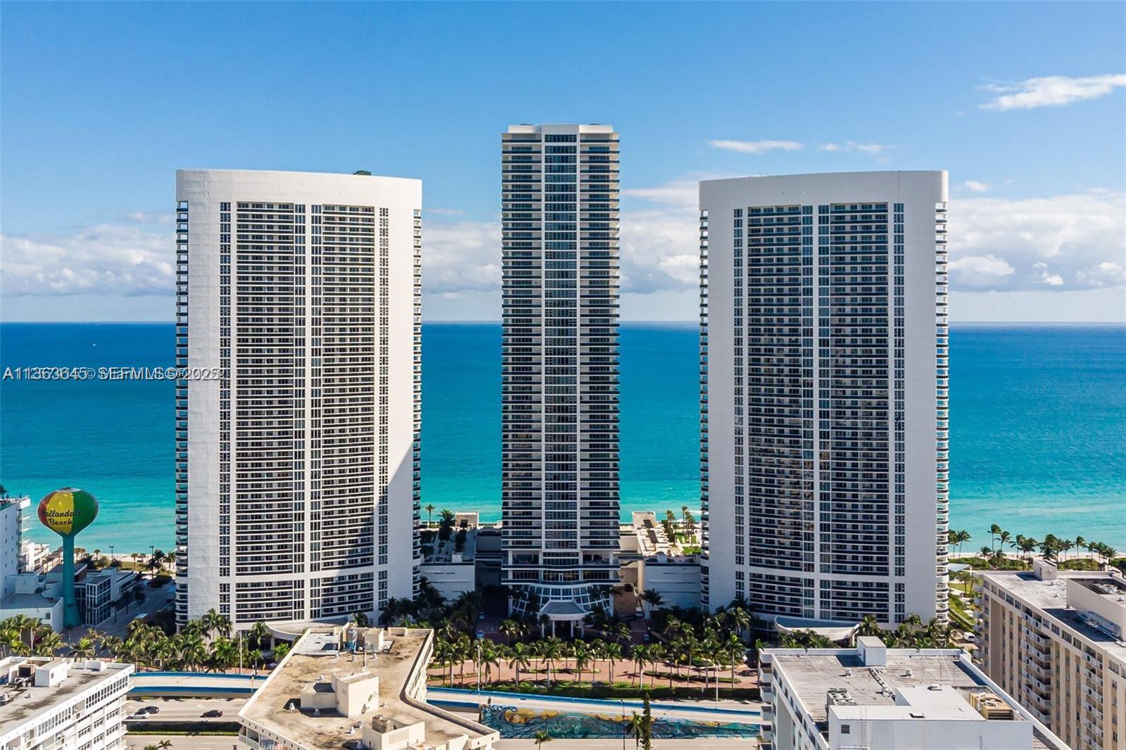 Three tall white residential towers stand along a beach with a water tower nearby — 1830 S Ocean Dr, Hallandale Beach FL 33009, HALLANDALE BEACH, FL