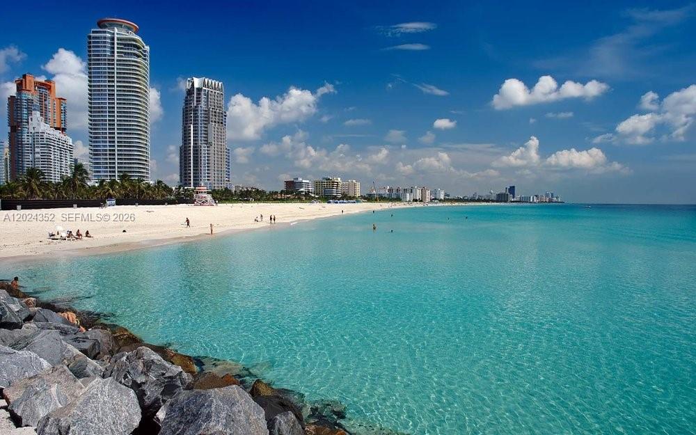 A view of a sandy beach with turquoise water and high-rise buildings in the background — 934 Meridian Ave # 7, Miami Beach FL 33139, MIAMI BEACH, FL