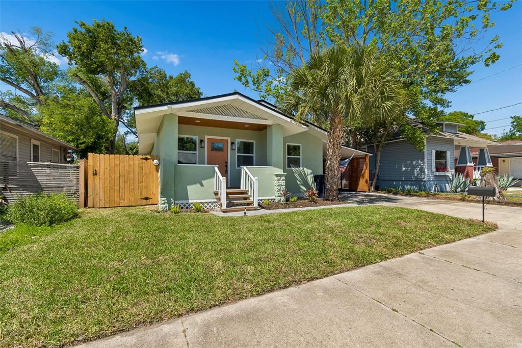 A light green bungalow with a front porch, wooden fence, and a palm tree — 106 E FERN STREET, TAMPA, FL