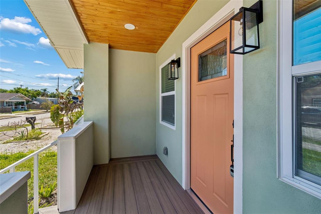 A covered front porch features a peach-colored door, wood-look decking, and light green exterior walls — 106 E FERN STREET, TAMPA, FL