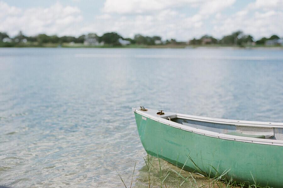 A green canoe rests on the sandy shore of a calm lake under a cloudy sky — 5906 Quince Road, Sebring FL 33875, SEBRING, FL