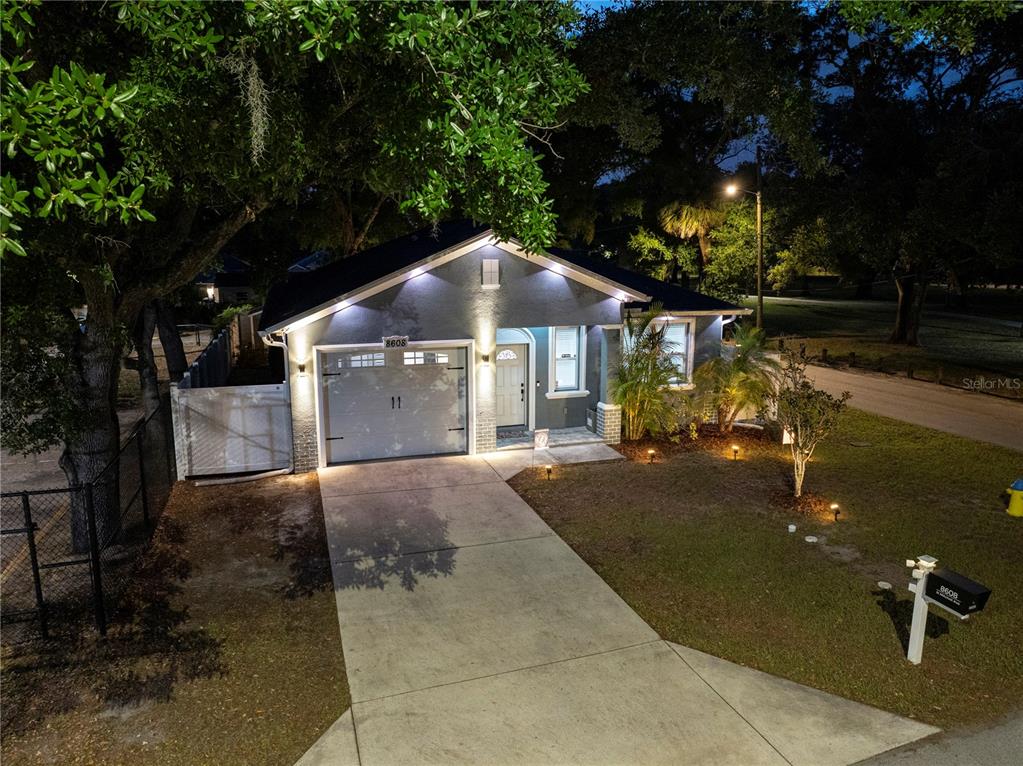 A single-story house with a gray exterior, a one-car garage, and a concrete driveway at night — 8608 N MITCHELL AVENUE, TAMPA, FL
