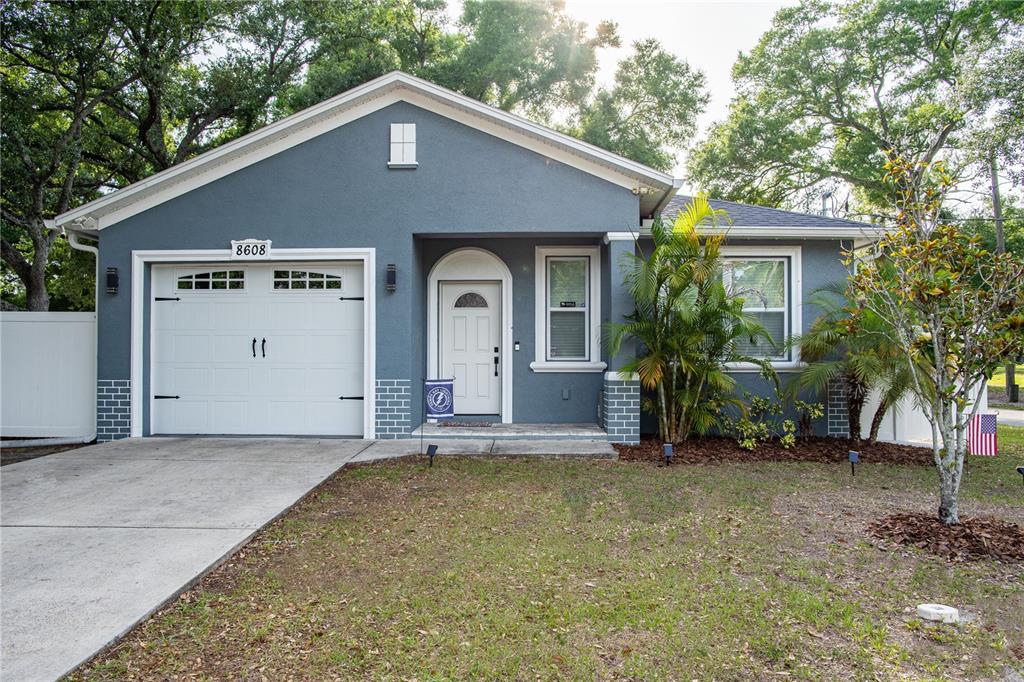 A gray single-story house with a white garage door, front porch, and a grassy yard — 8608 N MITCHELL AVENUE, TAMPA, FL