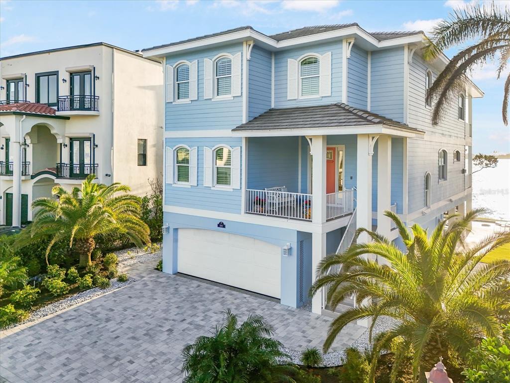 A light blue, three-story coastal home features a white garage, front porch, and palm trees — 12917 42ND TERRACE W, CORTEZ, FL