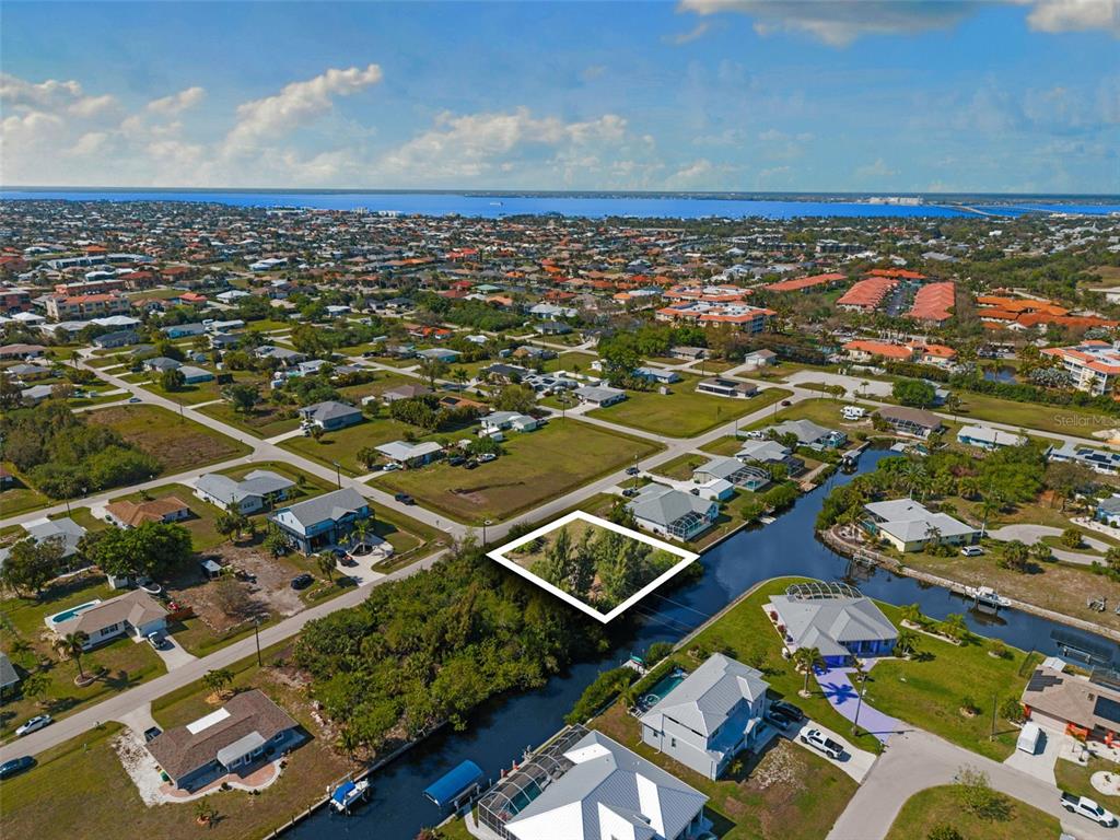 An aerial view shows a vacant, tree-covered waterfront lot outlined in white within a residential neighborhood — 2524 LARKSPUR DRIVE, PUNTA GORDA, FL