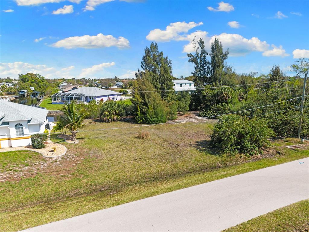 An elevated view of a vacant, grassy residential lot bordered by trees and nearby houses — 2524 LARKSPUR DRIVE, PUNTA GORDA, FL
