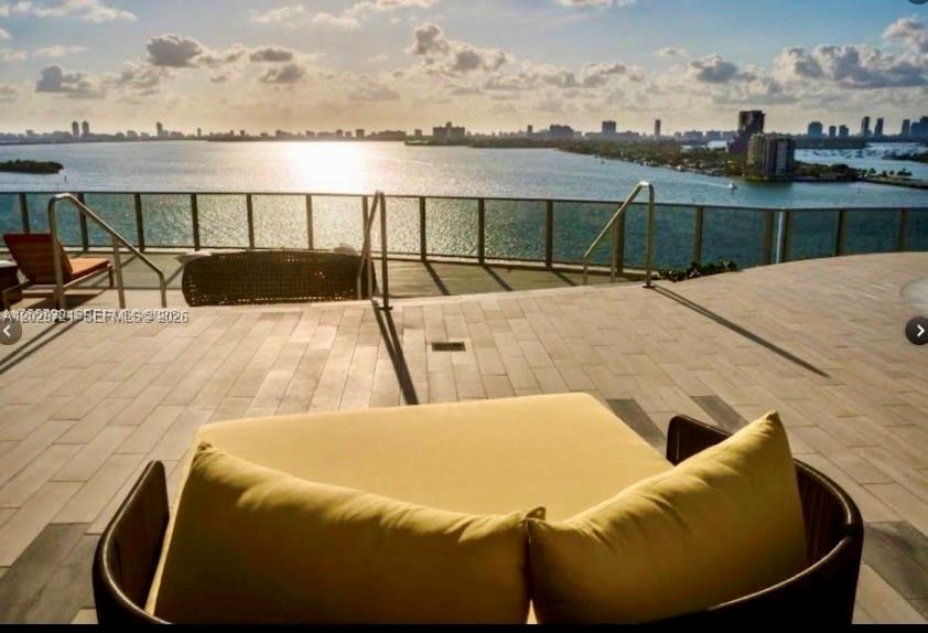 A balcony with outdoor furniture overlooks a bay and a distant city skyline — 488 NE 18th St # 705, Miami FL 33132, MIAMI, FL
