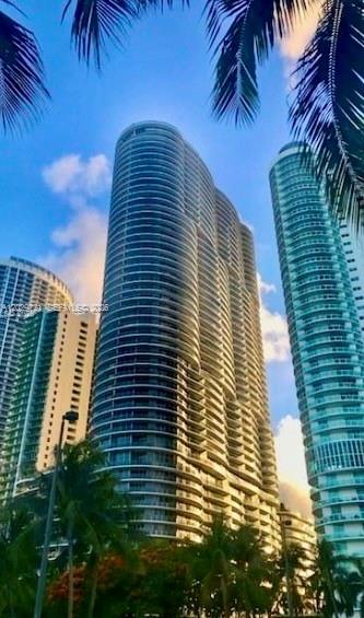 A low-angle view of several tall, modern glass skyscrapers framed by palm tree fronds — 488 NE 18th St # 705, Miami FL 33132, MIAMI, FL