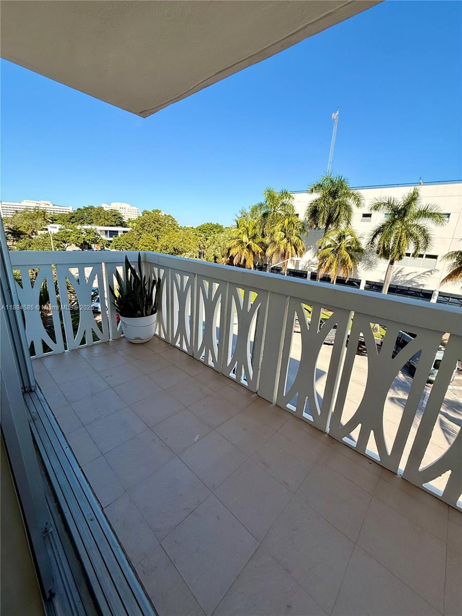 A balcony with a white lattice railing, tiled floor, and a potted plant overlooking trees — 4142 N Jefferson Ave # 4D, Miami Beach FL 33140, MIAMI BEACH, FL
