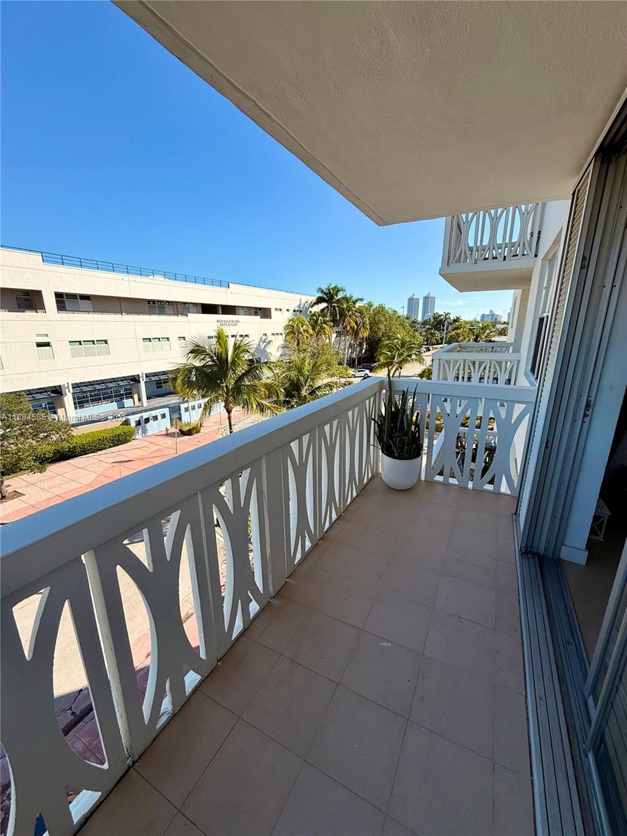 A balcony with white decorative railings overlooks a parking lot, palm trees, and distant buildings — 4142 N Jefferson Ave # 4D, Miami Beach FL 33140, MIAMI BEACH, FL