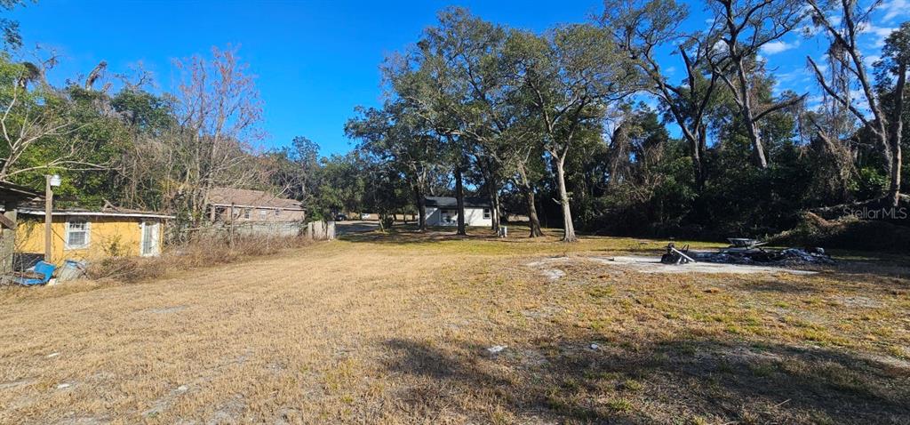 A grassy lot features a small yellow structure on the left and a white house behind trees — E CLEVELAND STREET, APOPKA, FL