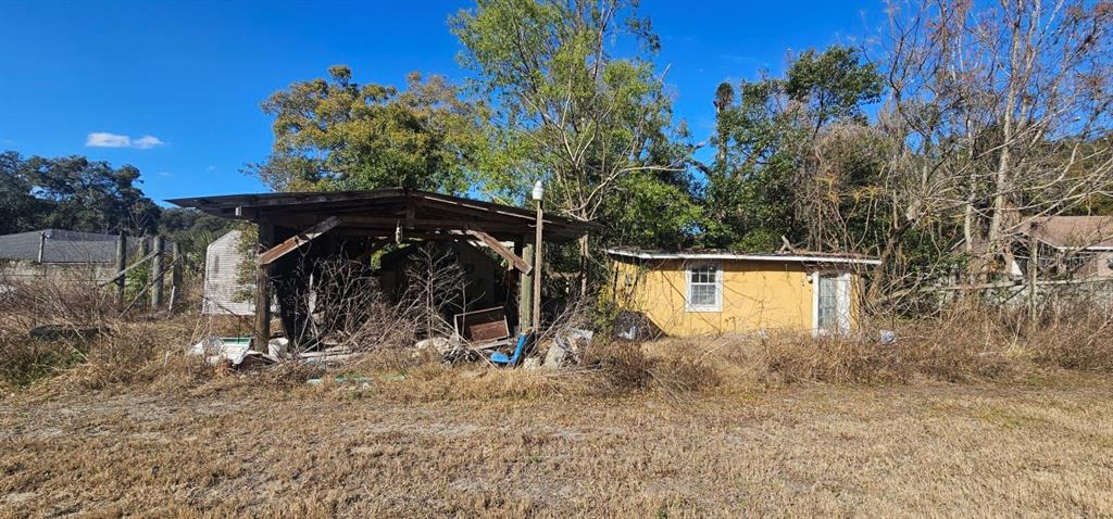An open-sided wooden carport stands next to a small, yellow, single-story building with overgrown vegetation — E CLEVELAND STREET, APOPKA, FL