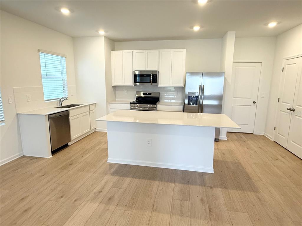 A kitchen features white cabinets, stainless steel appliances, a center island, and light wood flooring — 5107 LOYALTY DRIVE, ST CLOUD, FL