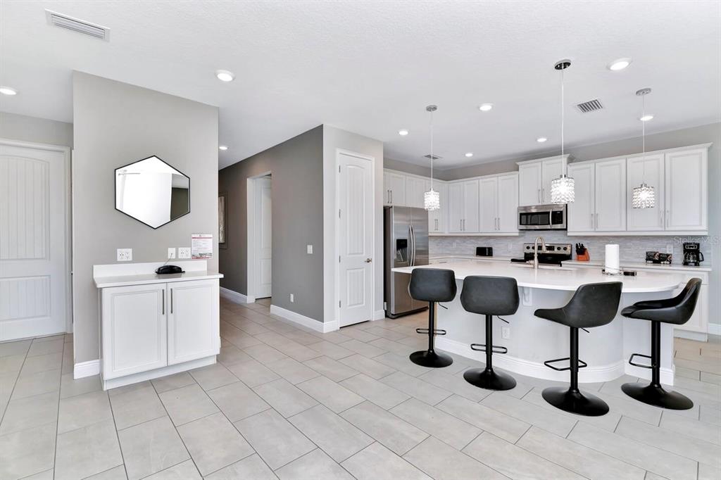 A modern kitchen features white cabinetry, a large island with four barstools, and tile flooring — 253 SOUTHFIELD STREET, KISSIMMEE, FL