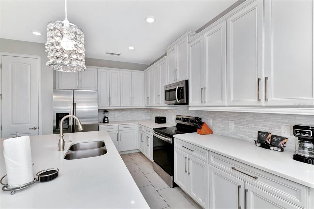 A modern kitchen features white cabinetry, stainless steel appliances, and a large island with seating — 253 SOUTHFIELD STREET, KISSIMMEE, FL
