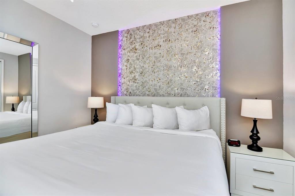 A bedroom features a king bed with a floral accent wall and purple LED lighting — 253 SOUTHFIELD STREET, KISSIMMEE, FL