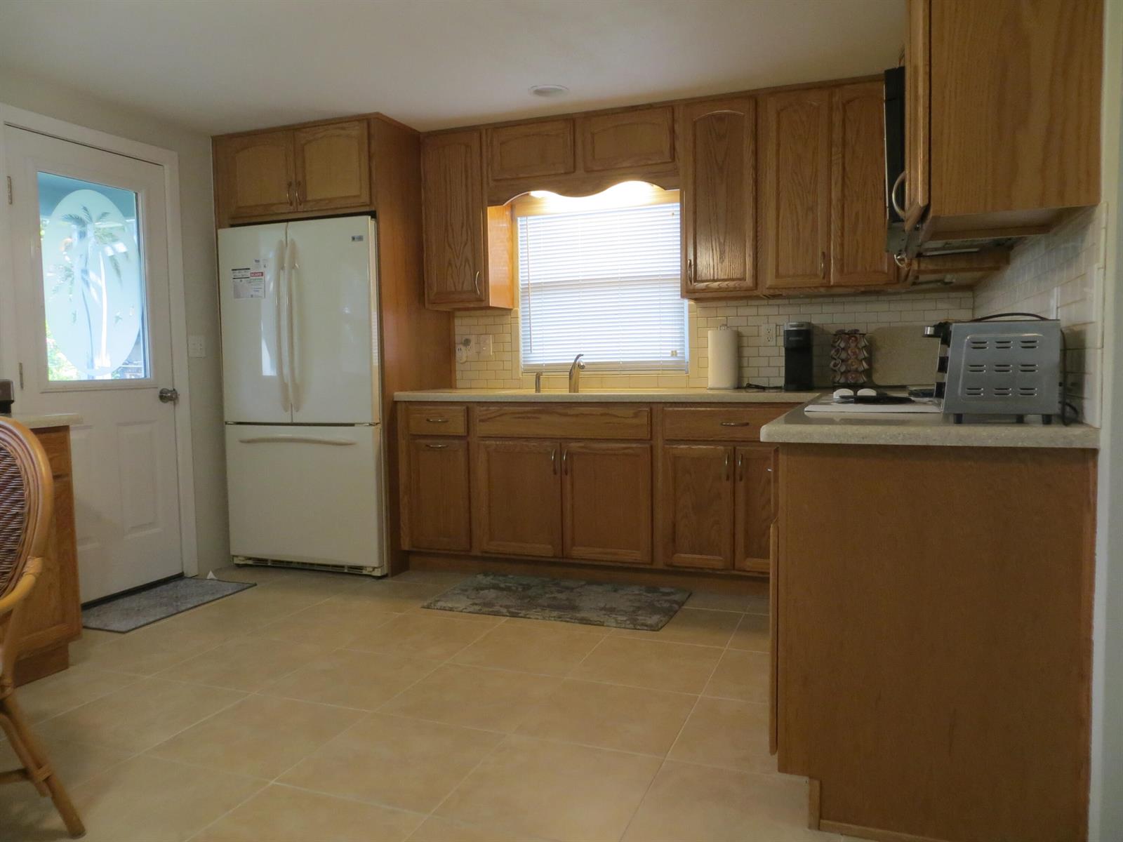 A kitchen with oak cabinets, white appliances, a tiled backsplash, and light-colored floor tiles — 509 S Mccall Road, Englewood FL 34223, ENGLEWOOD, FL