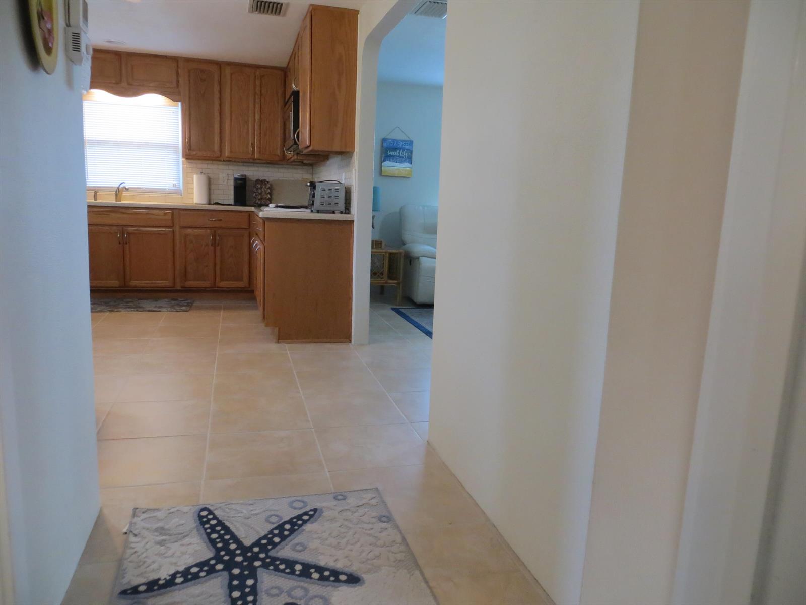 A view from a hallway into a kitchen with wood cabinets and tile flooring — 509 S Mccall Road, Englewood FL 34223, ENGLEWOOD, FL