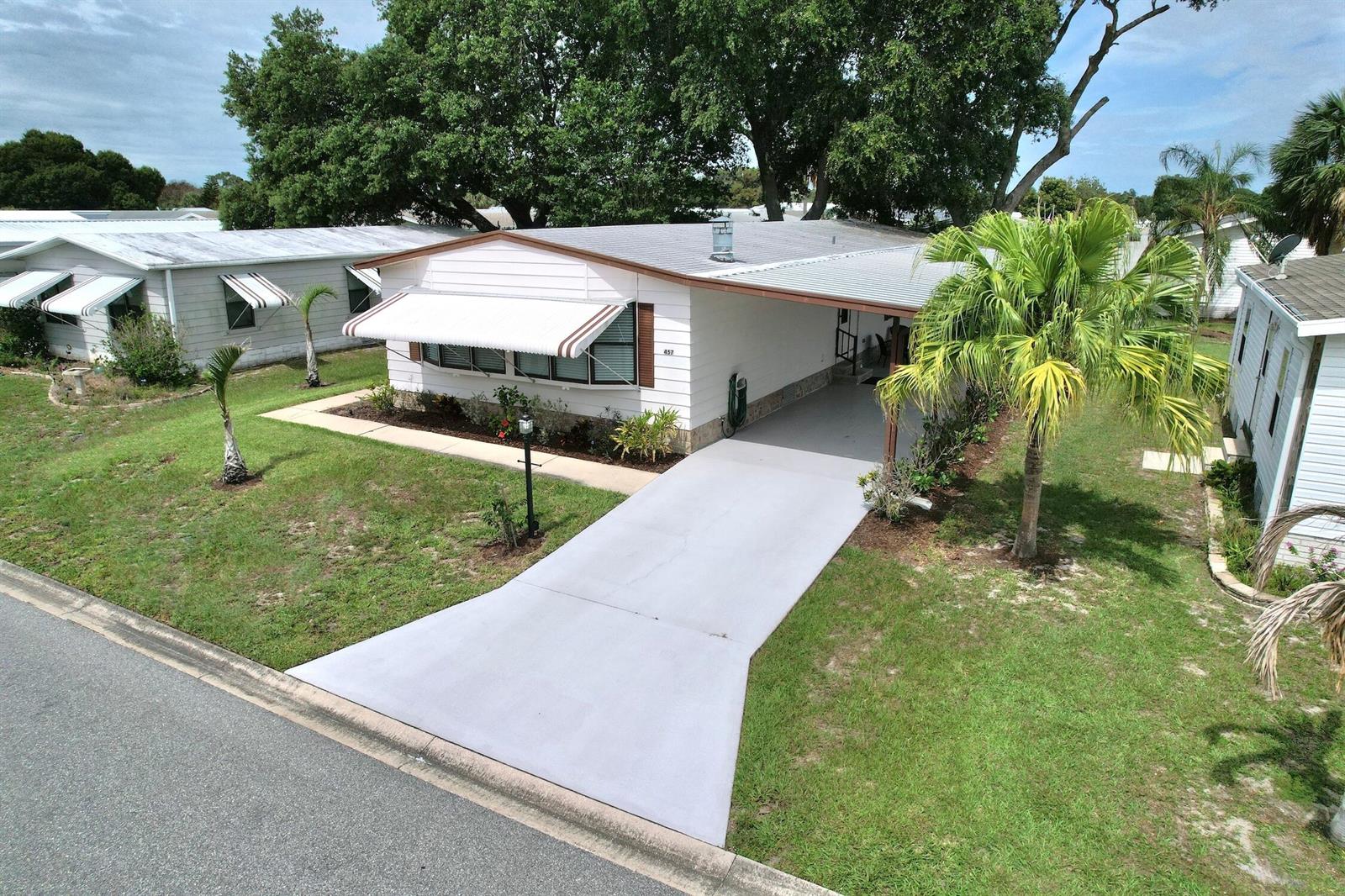 An elevated view of a white mobile home with a carport and a striped awning — BAREFOOT BAY, FL