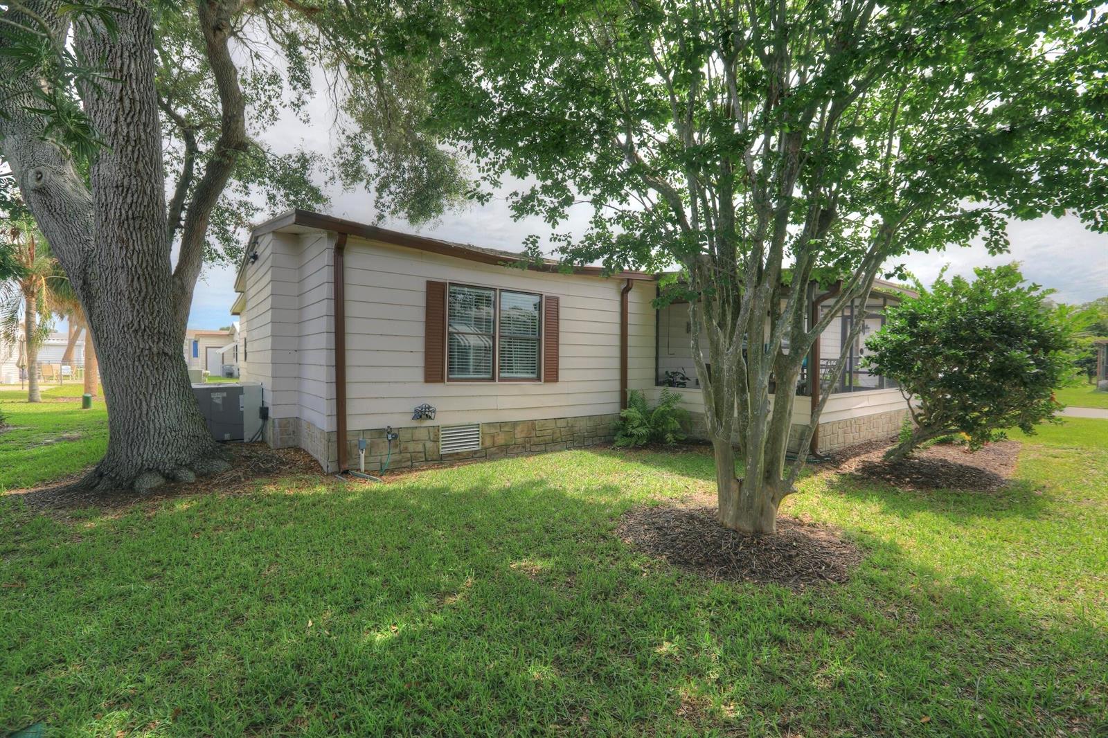 A single-story mobile home with tan siding, brown shutters, and a screened-in porch — BAREFOOT BAY, FL