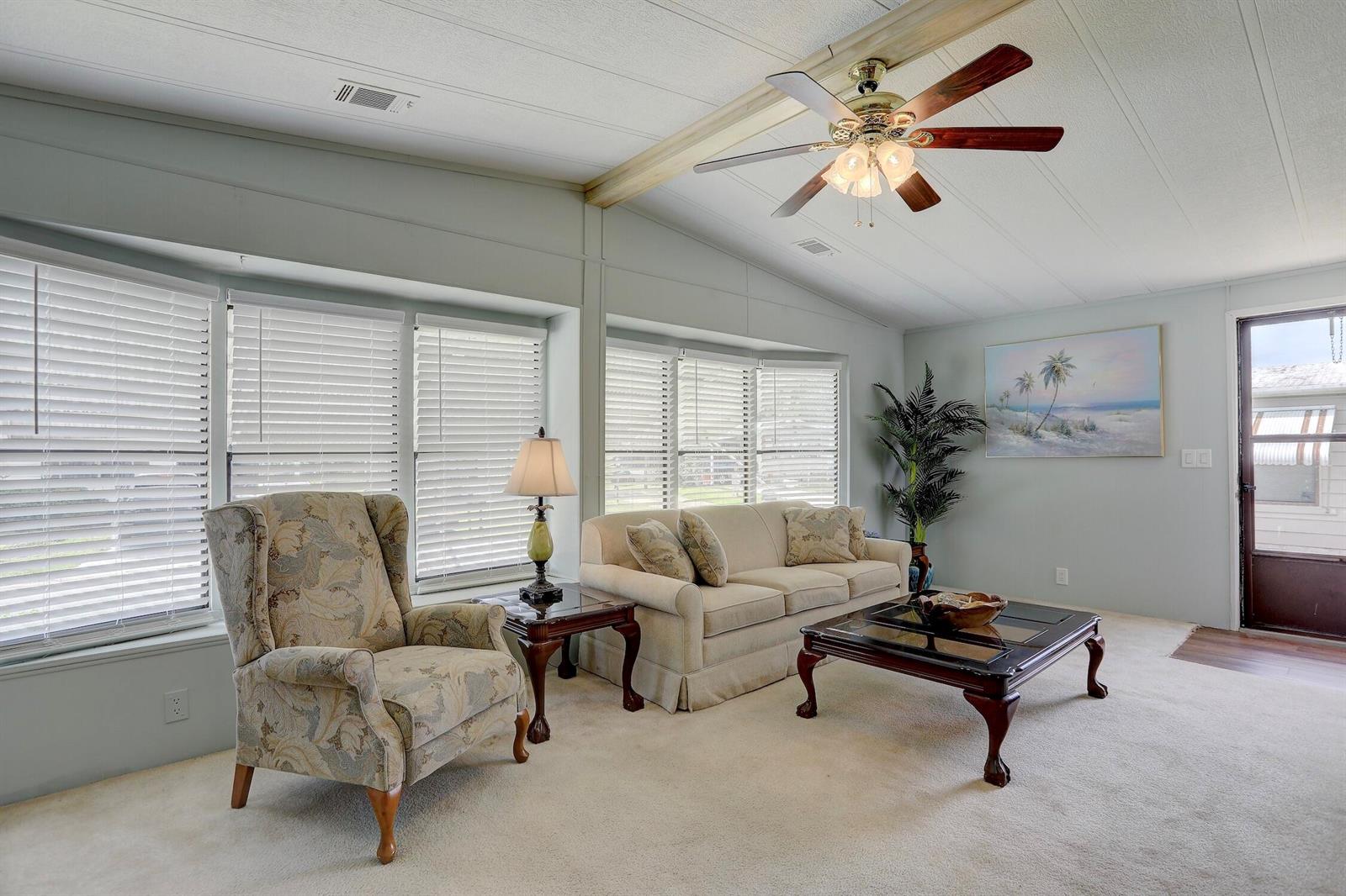 A living room features a beige sofa, patterned armchair, coffee table, and a ceiling fan — BAREFOOT BAY, FL