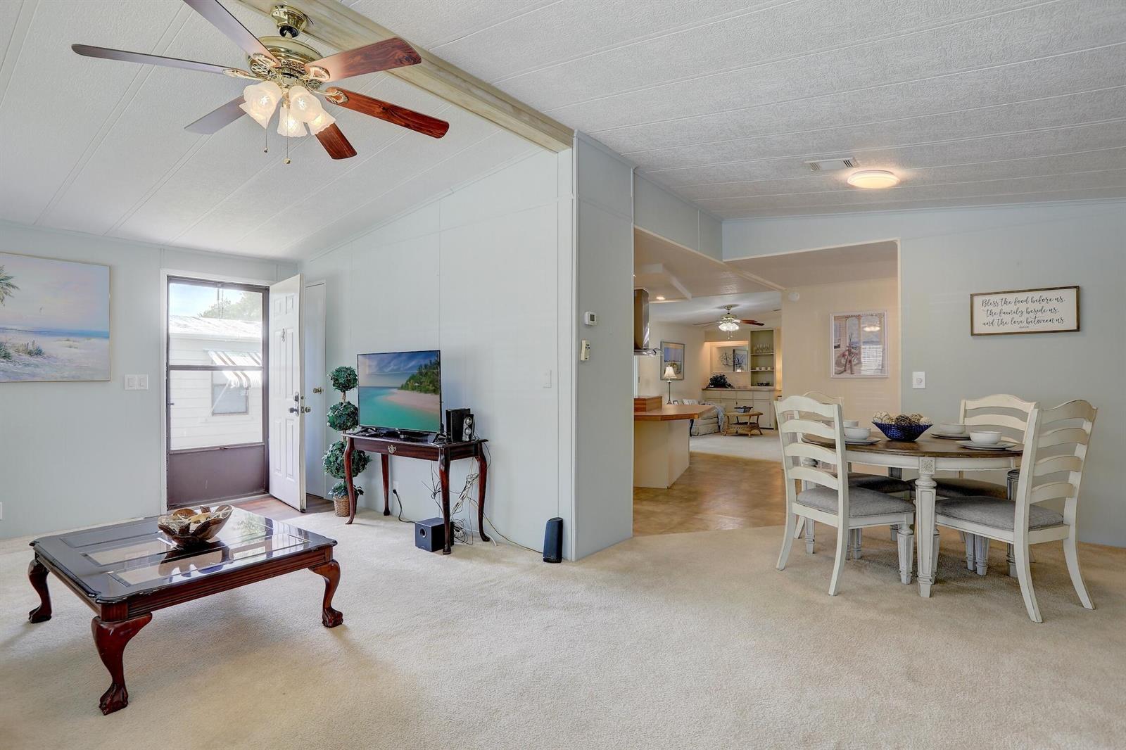 A living room with beige carpet, a ceiling fan, and a dining area in the background — BAREFOOT BAY, FL