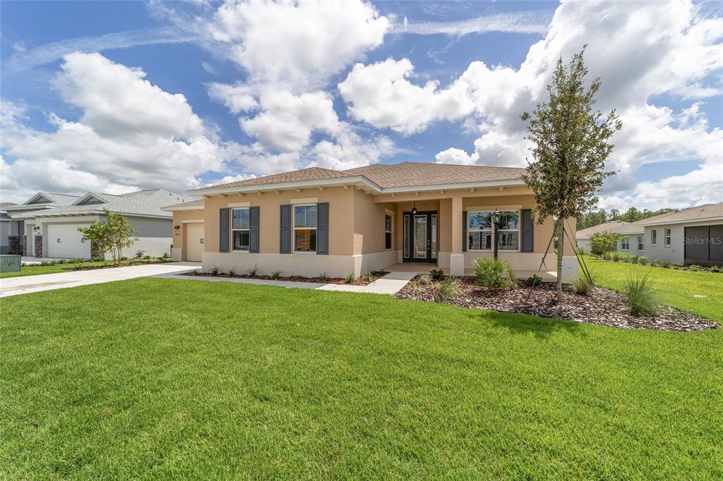 A tan, single-story suburban house with a brown roof, gray shutters, and a green lawn — 10135 SW 106TH CIRCLE, OCALA, FL