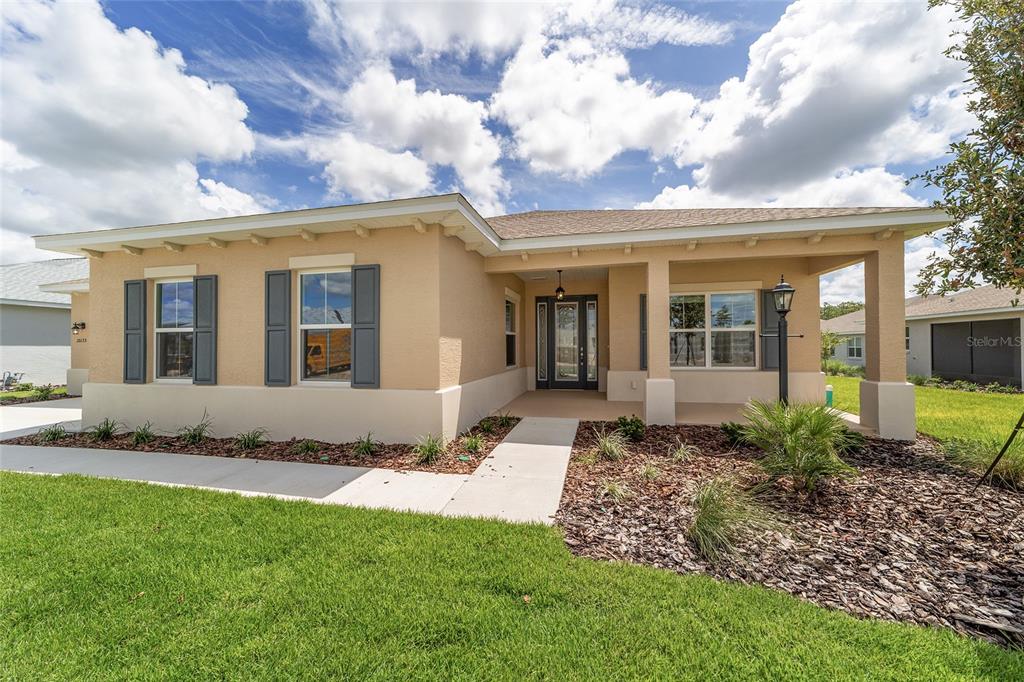 A single-story house with tan stucco walls, dark shutters, and a covered front porch — 10135 SW 106TH CIRCLE, OCALA, FL