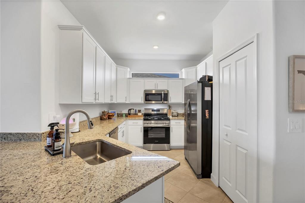A kitchen features white cabinets, granite countertops, stainless steel appliances, and a double-door pantry — 15733 SUNNY DAY DRIVE, BRADENTON, FL