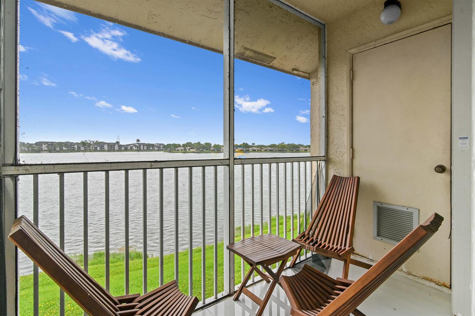 A screened-in balcony features three wooden chairs, a small table, and a lake view — 5530 Lakeside Drive # 203, Margate FL 33063, MARGATE, FL