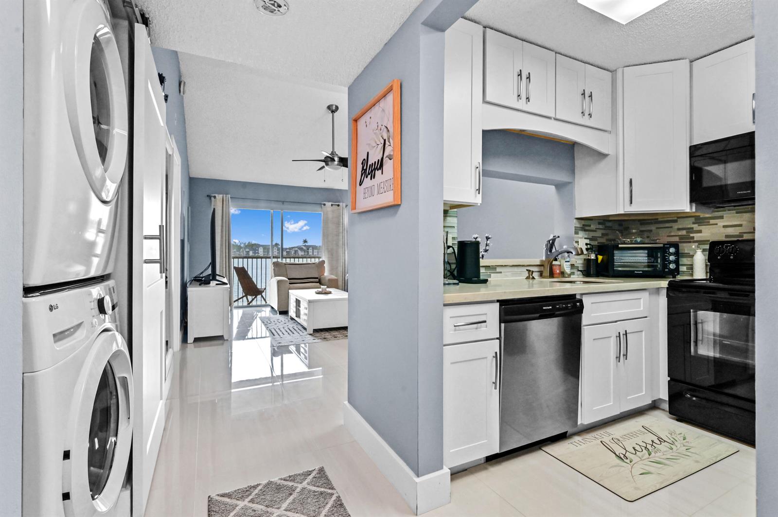 A kitchen with white cabinets and stainless appliances opens to a living area with balcony — 5530 Lakeside Drive # 203, Margate FL 33063, MARGATE, FL