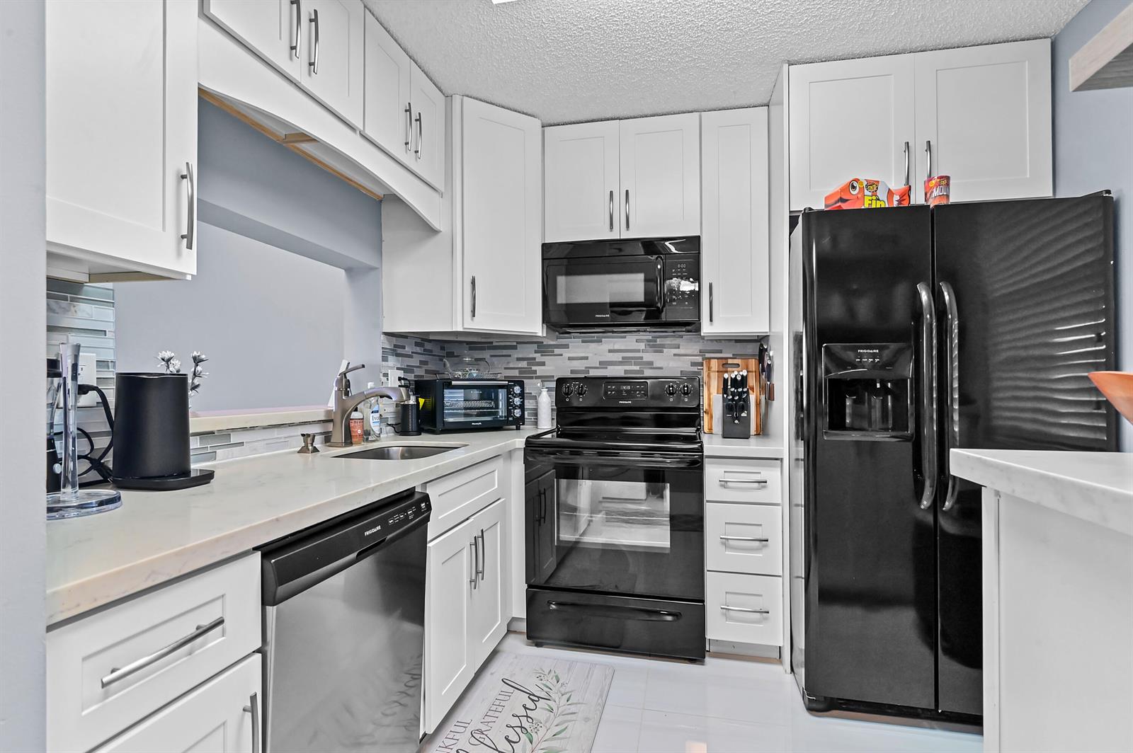A kitchen features white cabinets, black appliances, a stainless steel dishwasher, and light countertops — 5530 Lakeside Drive # 203, Margate FL 33063, MARGATE, FL
