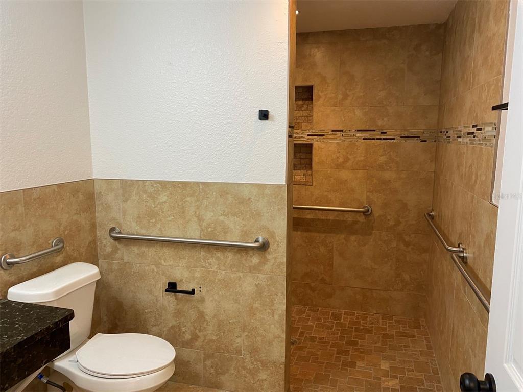 A bathroom features a toilet, a tiled walk-in shower with grab bars, and beige wall tiles — 1310 FAIRVIEW AVENUE, WINTER PARK, FL